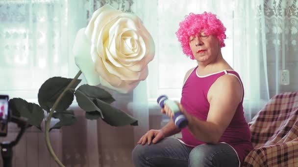 Gli uomini in parrucca rosa con trucco a casa scuotono i bicipiti dei manubri — Video Stock