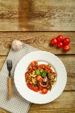 Ahşap bir masada, içinde mantar ve sebzeler olan kaynamış bir fasulye tabağı ve malzemelerin yanında da bir çatal var..