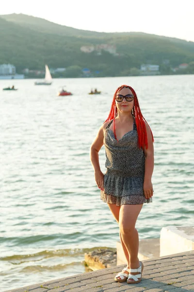 Vacker kvinna med rött hår står på en bakgrund av en fjällsjö. — Stockfoto