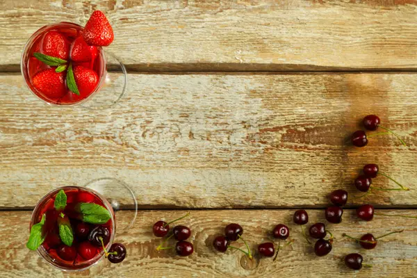 Два хрусталя с клубничным и вишневым соком, свежие ягоды и мята внутри на деревянном столе и ягоды на раме стола . — стоковое фото