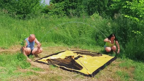 Een man en een vrouw op een open plek zetten een tent op, zetten een lijst op.. — Stockvideo