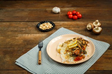 Tahta bir masanın üzerinde peçetenin üzerinde, tavuklu ve sebzeli bir tabak Tayland soslu ve mantarlı ve çatallı..