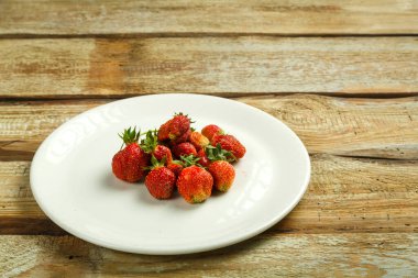 Tahta bir masada beyaz bir tabakta taze olgun çilek..