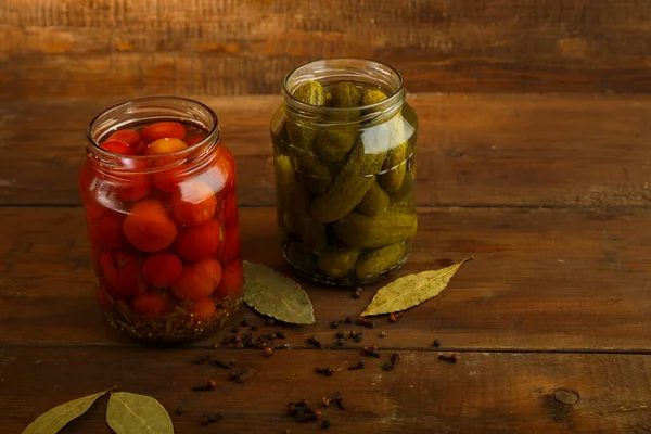 Burkar med inlagda hemmagjorda pickles och körsbärstomater och strödde kryddor på ett träbord. — Stockfoto