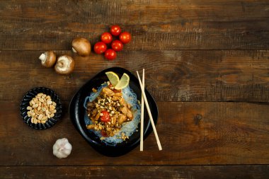 Tahta bir masanın üzerinde Tayland soslu tavuk ve sebze tabağı var.