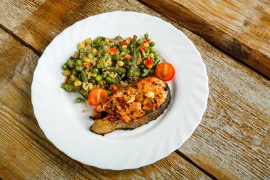 Ahşap bir masada pişmiş alabalık bifteği ve yanında sebzeli kinoa tabağı var..