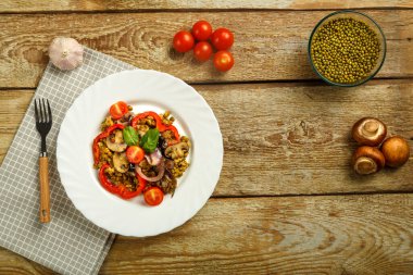 Ahşap bir masanın üzerinde, üzerinde sebze, peçete ve çatal üzerinde mantar bulunan bir fasulye yemeği var. Boşluğu kopyala.