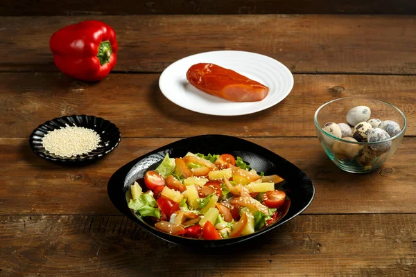 Pan-Aziatische salade met in een zwarte plaat en een rij ingrediënten op een houten tafel. — Stockfoto