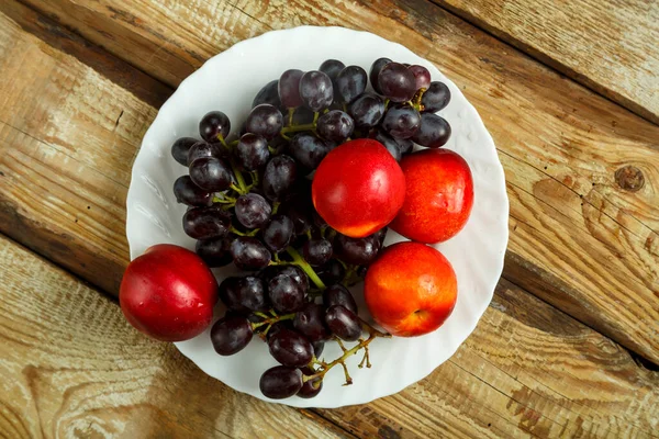 Виноград и персики на белой тарелке на столе. — стоковое фото