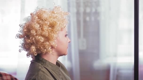 Μια γυναίκα μπροστά από έναν καθρέφτη φοράει μια περούκα κλόουν με γκρίζες μπούκλες. — Αρχείο Βίντεο
