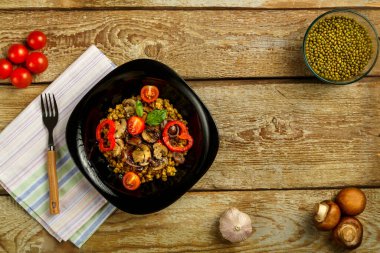 Ahşap bir masanın üzerinde siyah bir tabak haşlanmış fasulye, peçete ve çatal üzerinde sebze ve mantar var. Boşluğu kopyala.