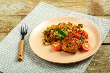 Fırınlanmış tavuk göğsü, domates ve sebzelerle süslenmiş, çatallı bir tabakta, peçeteyle..