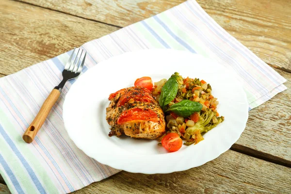 Baharatlı tavuk göğsü, yanında sebze tabağı ve keten peçetedeki çatalla birlikte beyaz tabakta..