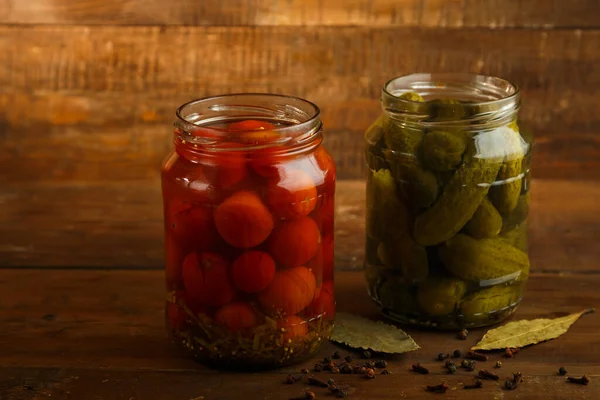 Frascos de pepinos en escabeche y tomates caseros y especias espolvoreadas sobre una mesa de madera . —  Fotos de Stock