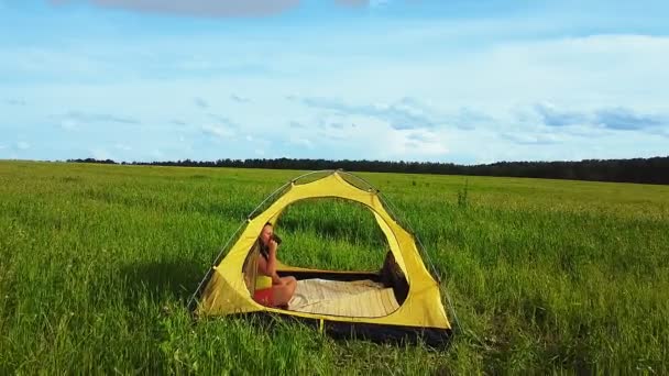 Kvinnan i ett tält i en glänta en solig dag. Kamerans passage genom tältet — Stockvideo