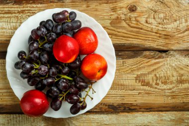 Masadaki beyaz tabakta üzüm ve şeftali. Boşluğu kopyala.