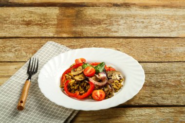 Ahşap bir masanın üzerinde beyaz bir tabak haşlanmış mung fasulyesi, peçete ve çatal üzerinde sebzeler ve mantarlar var. Boşluğu kopyala.