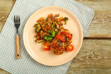 Fırınlanmış tavuk göğsü, domates ve sebzelerle süslenmiş, çatallı bir tabakta, peçeteyle..