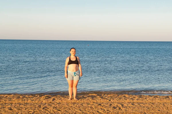 Una chica en pantalones cortos y una parte superior está de pie en la orilla del mar . — Foto de Stock