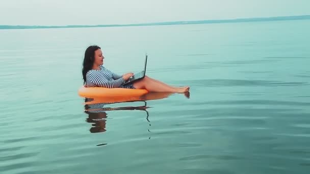 Деловая женщина на отдыхе в резиновом кольце плавает у моря утром и работает на ноутбуке. — стоковое видео