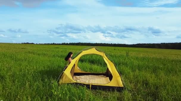 En kvinna nära ett tält i en grön glänta dricker te. — Stockvideo