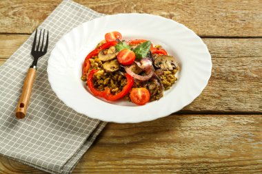 Ahşap bir masanın üzerinde beyaz bir tabak haşlanmış mung fasulyesi mantarlı ve sebzeli bir peçete ve bir çatal var..