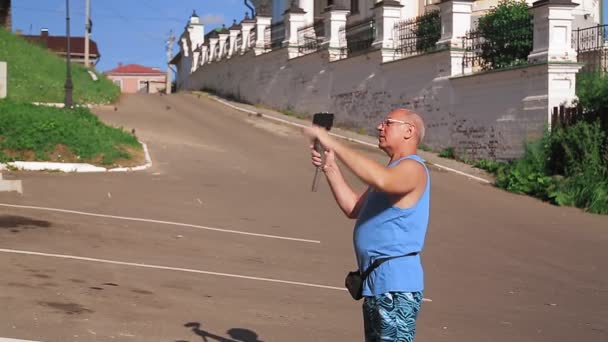 Un blogueur masculin avec un téléphone portable parle de voyager dans une petite vieille ville. — Video