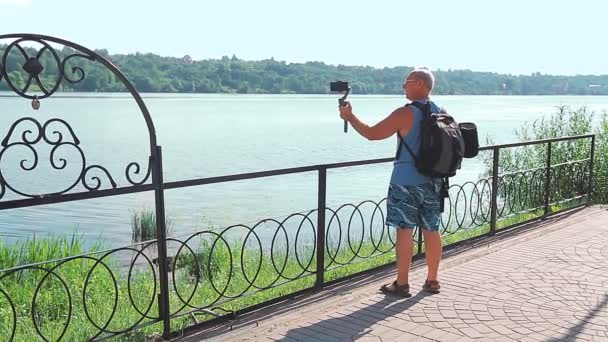Męski bloger z telefonem komórkowym o podróżach mówi o nabrzeżu małego miasteczka. — Wideo stockowe
