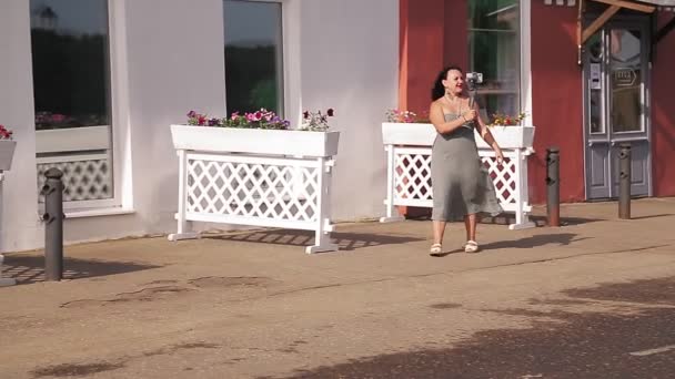 Een vrouw op reis blogger loopt door een straat en blogs van haar mobiele telefoon. — Stockvideo