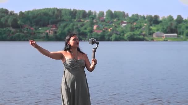 Žena blogger s mobilním telefonem je blogování z břehu řeky. — Stock video