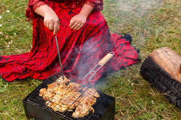 Uma mulher cigana elegante verifica a prontidão da carne grelhada . — Fotografia de Stock