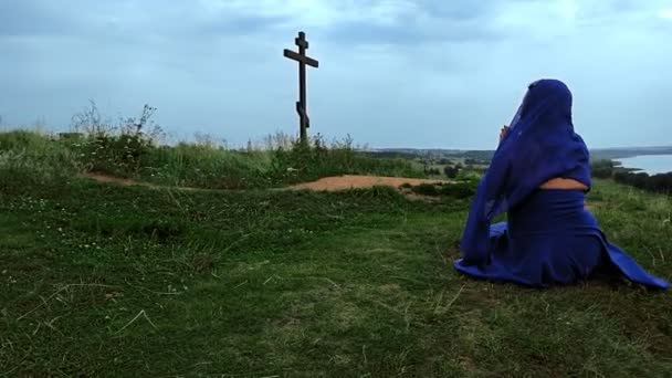 Uma peregrina de azul e uma capa na cabeça reza no topo da montanha — Vídeo de Stock