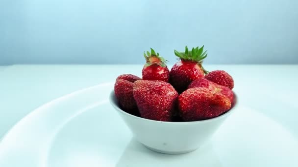 Een bord met rijpe aardbeien draait in een cirkel op een witte achtergrond. — Stockvideo