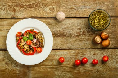 Ahşap bir masada, içinde mantar ve sebzeler bulunan kaynamış bir fasulye tabağı var..