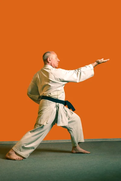 A karate man in a white kimono with a black belt performs kata getting ready for the competition.