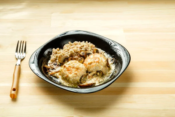 Куриные фрикадельки с грибами в сливочном соусе с гарниром из зеленой гречихи в тарелке с вилкой. — стоковое фото