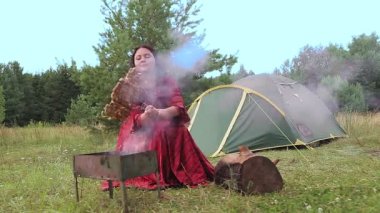 Genç ve zeki bir çingene kadın çadırın yanındaki açıklıkta et pişiriyor..