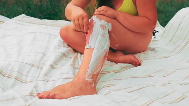Una mujer sin rostro en un claro en una sábana se afeita las piernas con una navaja — Vídeo de stock