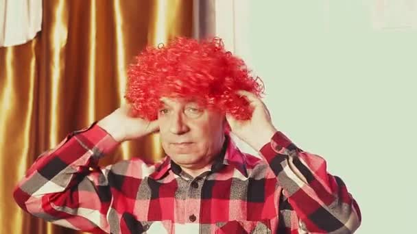 Un homme drôle danse dans une perruque de carnaval avec des boucles rouges. — Video