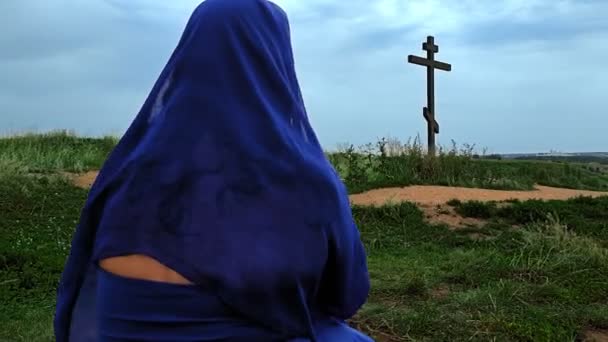 A female pilgrim in blue and a cape on her head prays on the top of the mountain — Stock Video