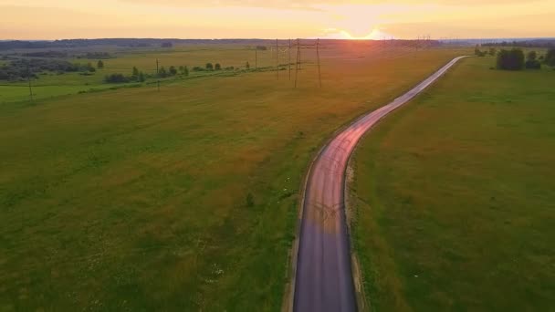 Дорога почти без автомобилей в сельской местности в середине поля на закате и высоковольтных линий. — стоковое видео