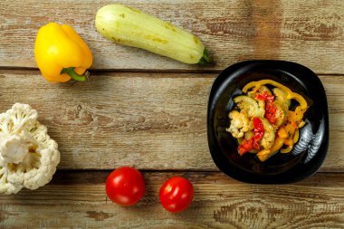 Siyah tabakta sebze yahnisi ve ahşap bir masada birkaç sebze..