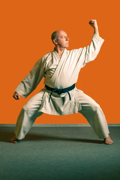 Ein Karate-Mann im weißen Kimono mit schwarzem Gürtel macht Kata-Übungen. — Stockfoto