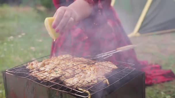 En ung smart zigenarkvinna i en glänta lägger kött på grillen och häller upp det med citronsaft — Stockvideo