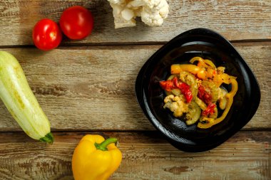 Siyah bir tabakta sebze yahnisi ve ahşap bir masada birkaç sebze..