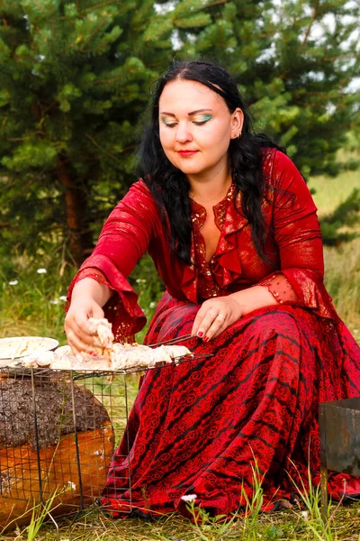 Una joven gitana pone carne en la parrilla junto al fuego . —  Fotos de Stock