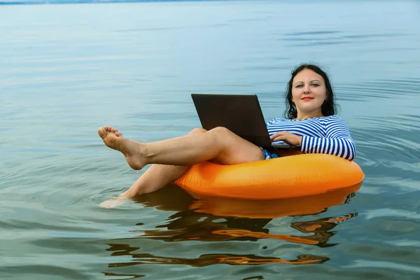 Woman works remotely with laptop in a swimming circle in water. — Stock Photo, Image