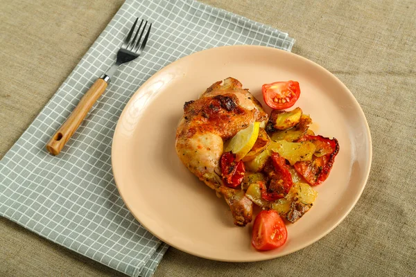 在叉子和餐巾旁边的桌布上放着土豆和西红柿的烤鸡腿. — 图库照片