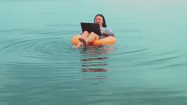 Jeune femme d'affaires en vacances dans un anneau en caoutchouc nage près de la mer le matin et travaille dans un ordinateur portable — Video