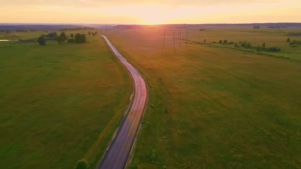 Вечірня дорога в сільській місцевості посеред поля під час заходу сонця і високовольтних ліній . — стокове відео